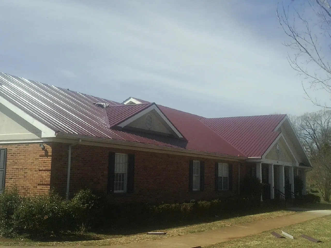 Red metal roof with gabled entries on a long brick building, from a Hail Damage Roof Repair job in Mattawa