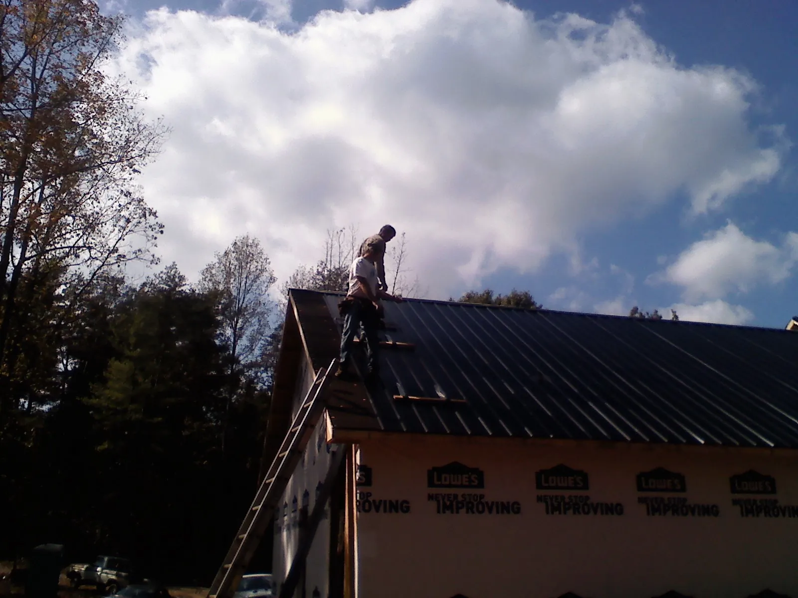 Roofer fastening dark metal panels high against a cloudy sky, from a Roof Inspection job in Mattawa