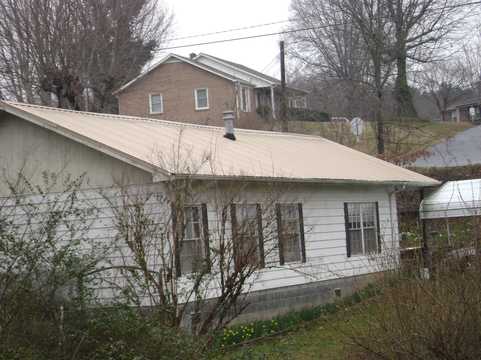 Tan metal roof on a white sided house set into a hillside — Commercial Roofing by Roofing Brothers in Mattawa